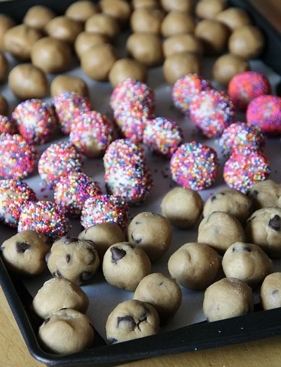 A variety of cookie dough balls with chocolate chips and rainbow sprinkles on a baking sheet