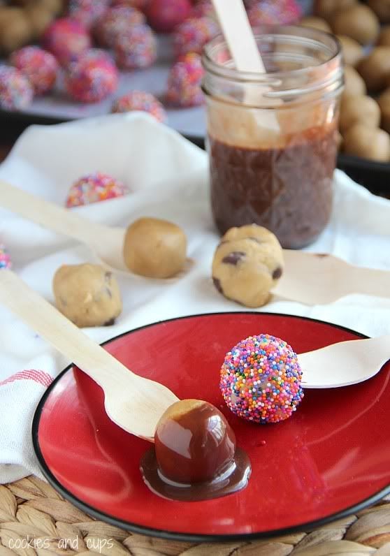 Cookie dough balls with sprinkles and melted chocolate on a plate next to a jar of melted chocolate