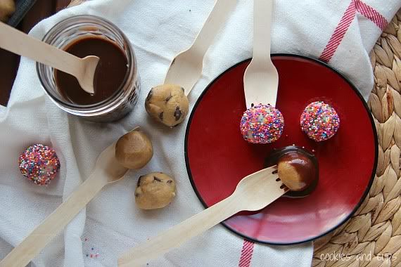 Top view of cookie dough balls with forks on a plate next to a cup of melted chocolate