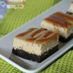 Close-up of brownie-bottom cheesecake bars with caramel drizzle on a platter