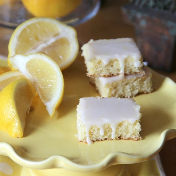 Three lemonade brownies next to a lemon wedge on a yellow plate.