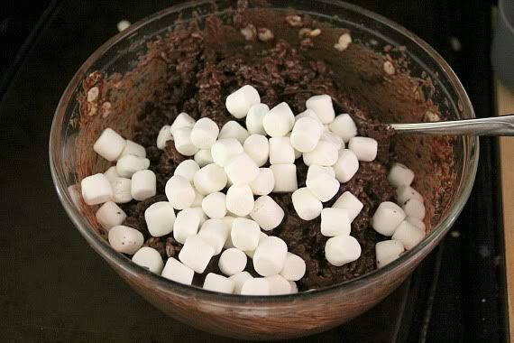 Mini marshmallows added to a bowl of melted chocolate and cereal mixture