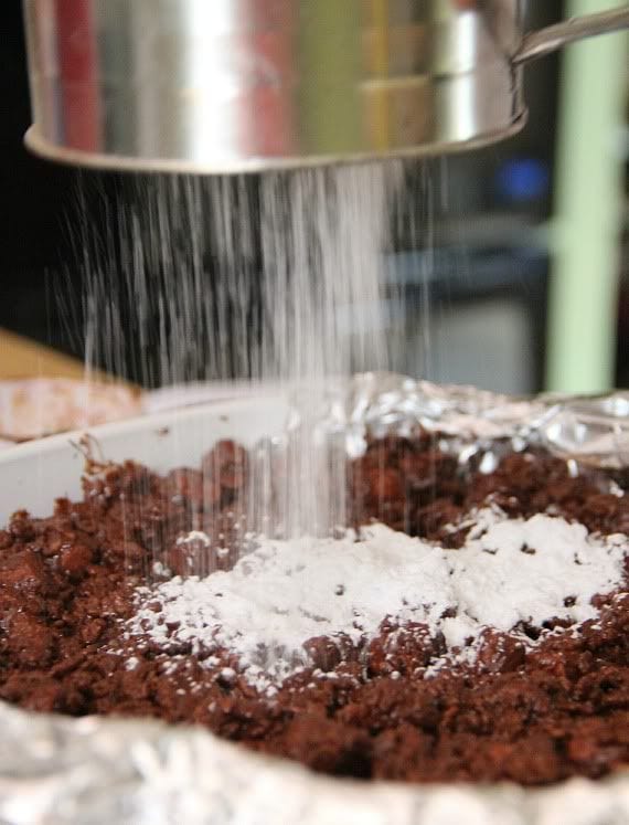 Powdered sugar being sifted over a square pan of chocolate krispie treats