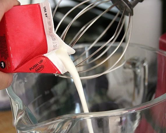 Heavy cream being poured into a stand mixer with whisk attachement