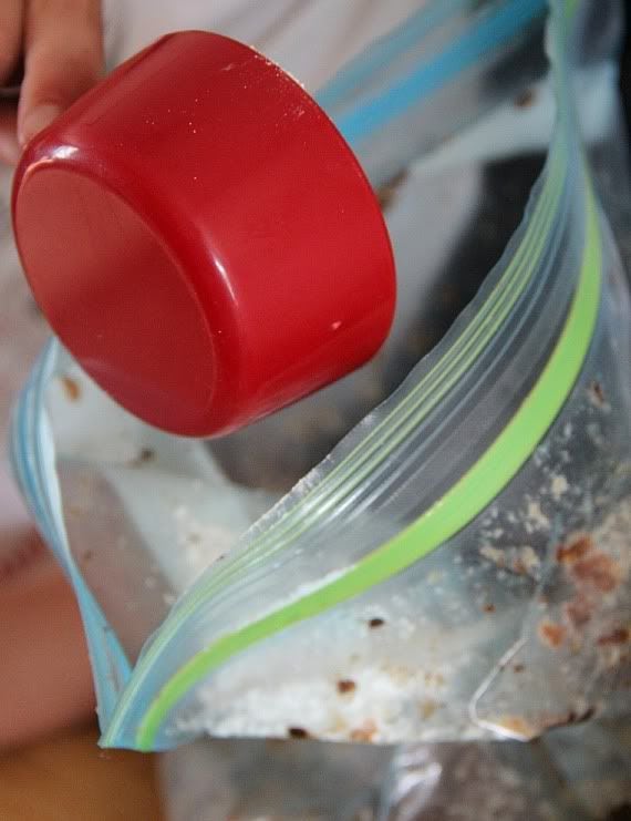 A measuring cup scooping crushed cookies out of a bag