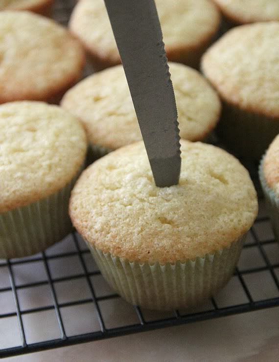 A knife sticking into a vanilla cupcake on a cooling rack