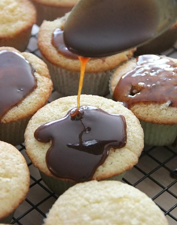 Caramel sauce being drizzled over vanilla cupcakes on a cooling rack