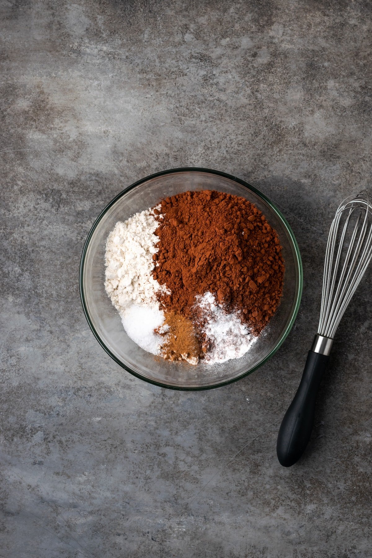 Dry brownie ingredients combined in a bowl next to a whisk.