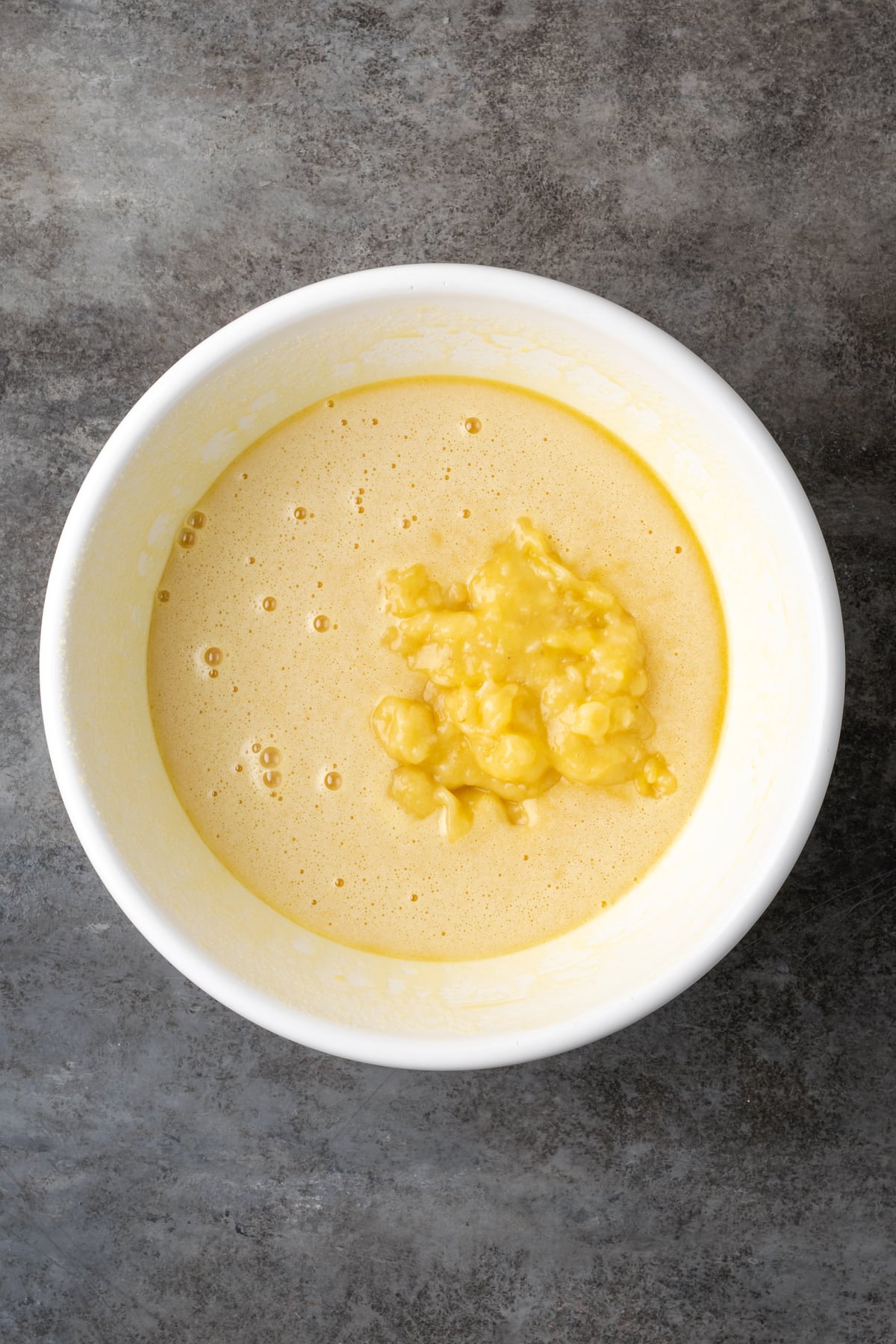 Mashed banana added to wet batter ingredients in a mixing bowl.