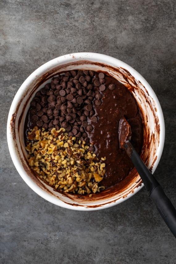 Chopped nuts added to banana bread brownie batter in a mixing bowl with a spoon.