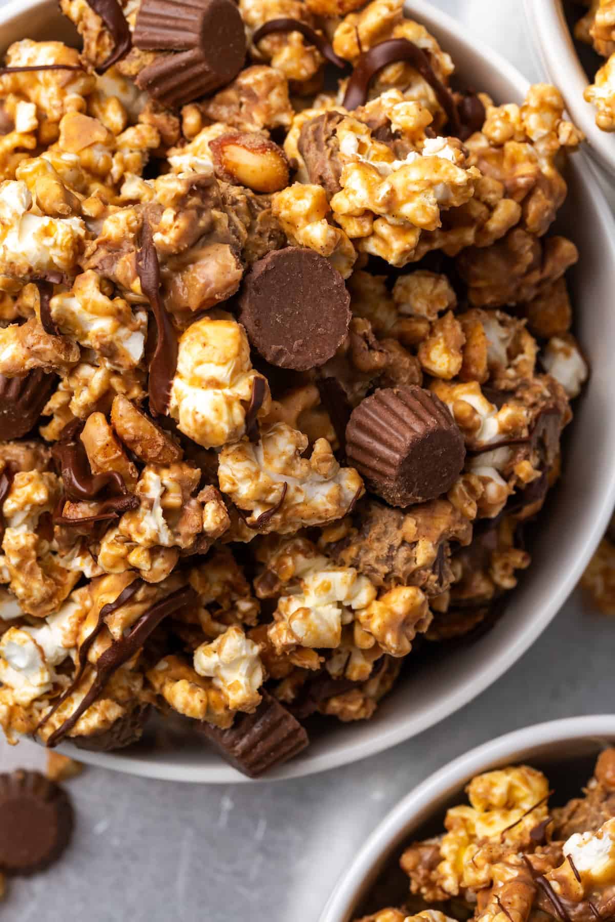 Peanut butter popcorn turns microwave popcorn into the ultimate sweet snack, tossed with peanut butter cups and drizzled with chocolate! Overhead view of peanut butter popcorn in a white bowl.