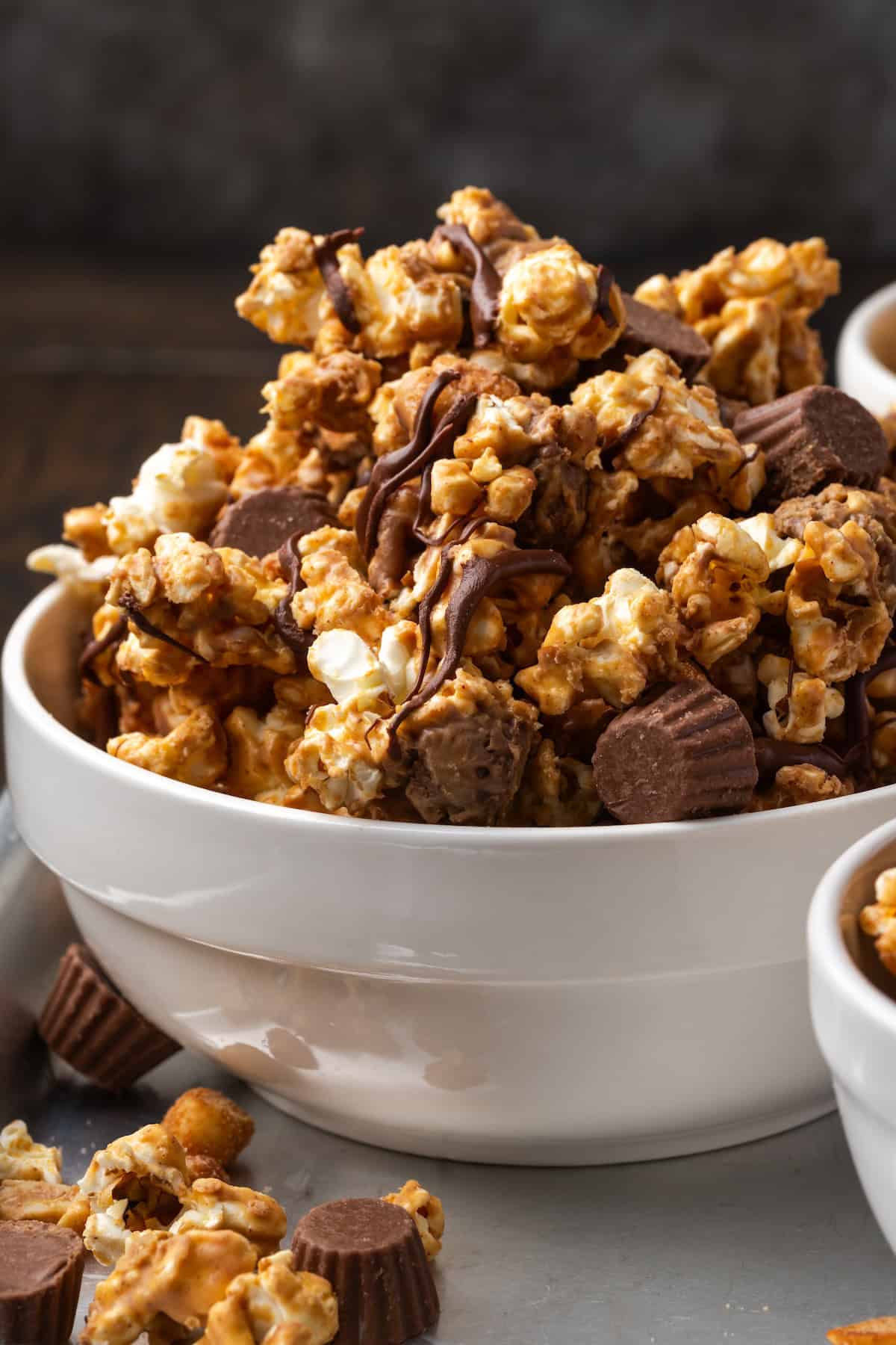 Peanut butter popcorn turns microwave popcorn into the ultimate sweet snack, tossed with peanut butter cups and drizzled with chocolate! Side view of peanut butter popcorn in a white bowl.