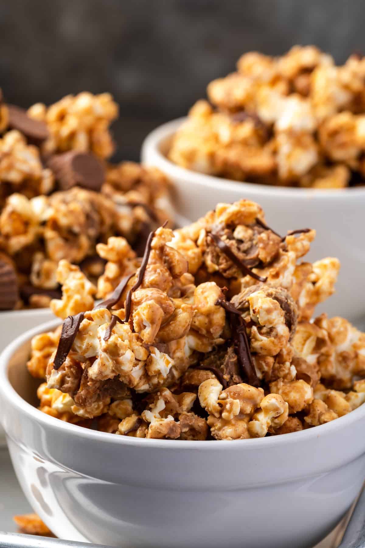 Peanut butter popcorn turns microwave popcorn into the ultimate sweet snack, tossed with peanut butter cups and drizzled with chocolate! Side view of peanut butter popcorn in white bowls.