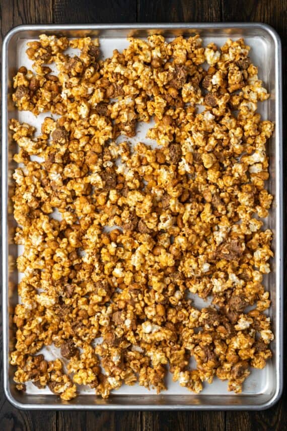 Peanut butter popcorn mixture spread onto a lined baking sheet.