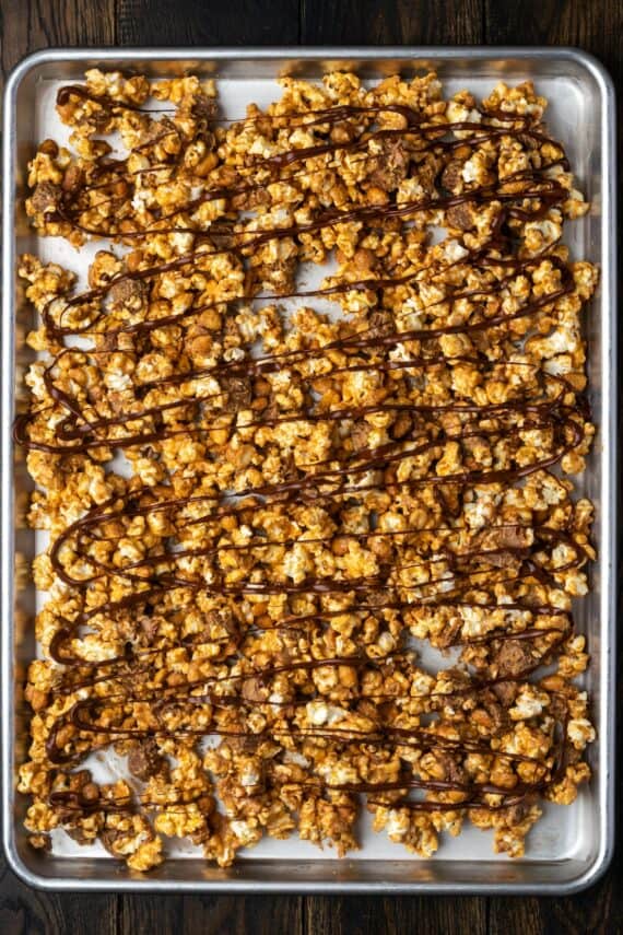 Peanut butter popcorn drizzled with melted chocolate on a lined baking sheet.