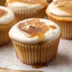 Salted caramel cupcakes on a parchment-lined wooden cutting board.