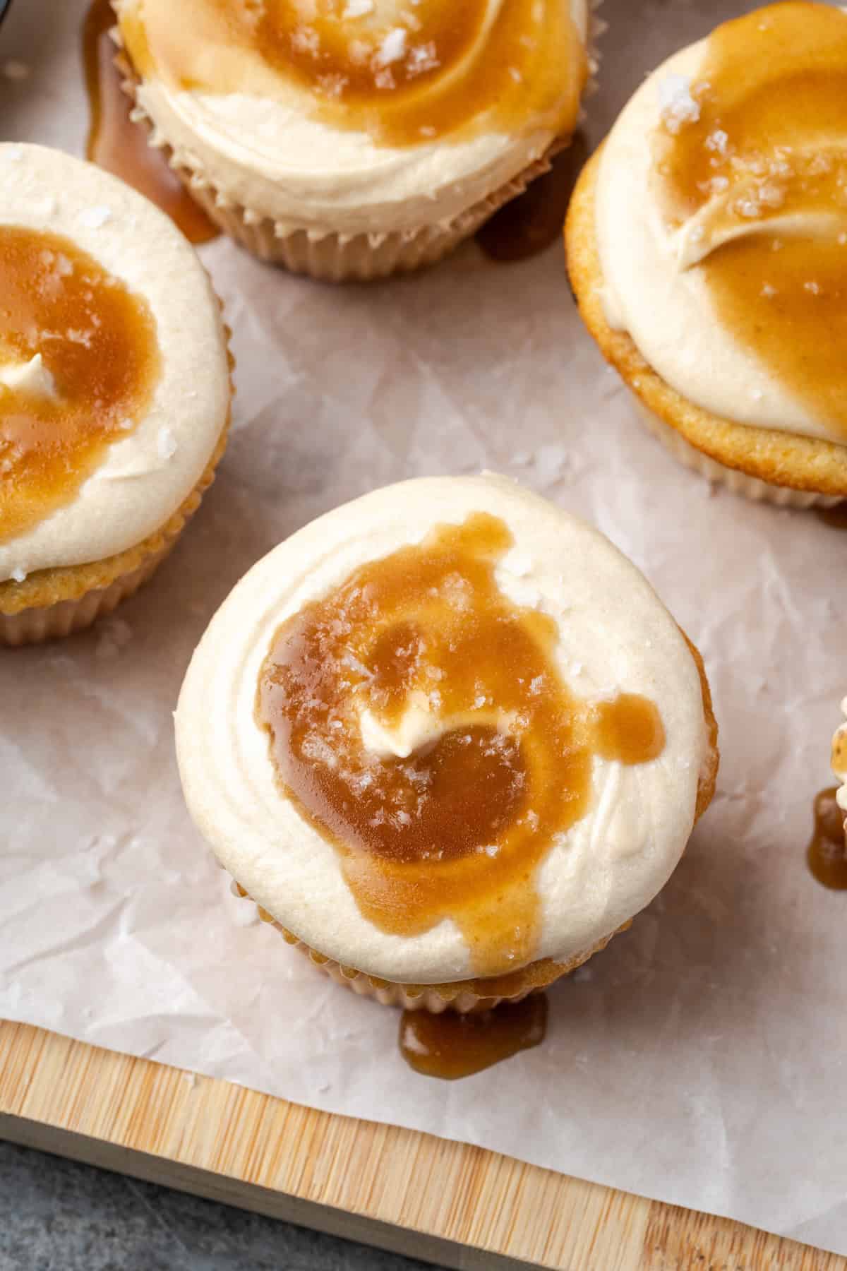 Overhead view of salted caramel cupcakes on a parchment-lined wooden cutting board.