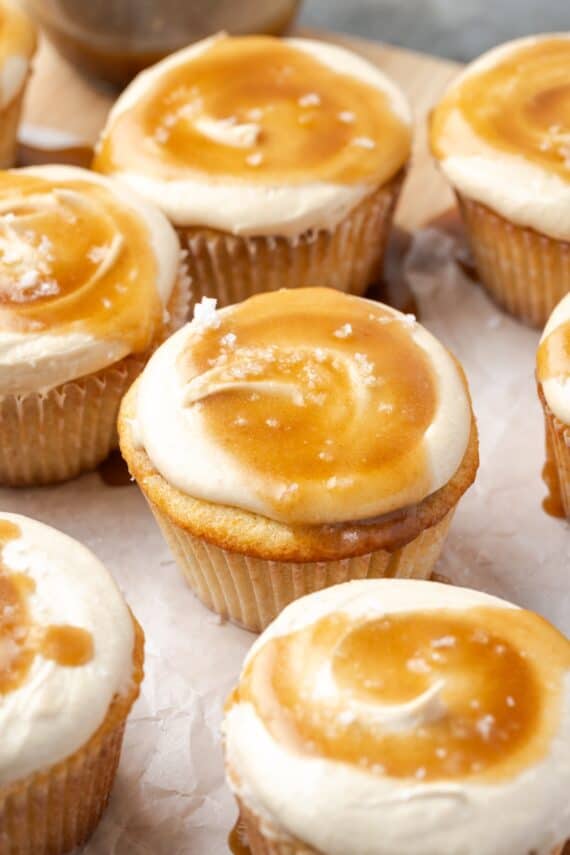 Salted caramel cupcakes on a parchment-lined wooden cutting board.