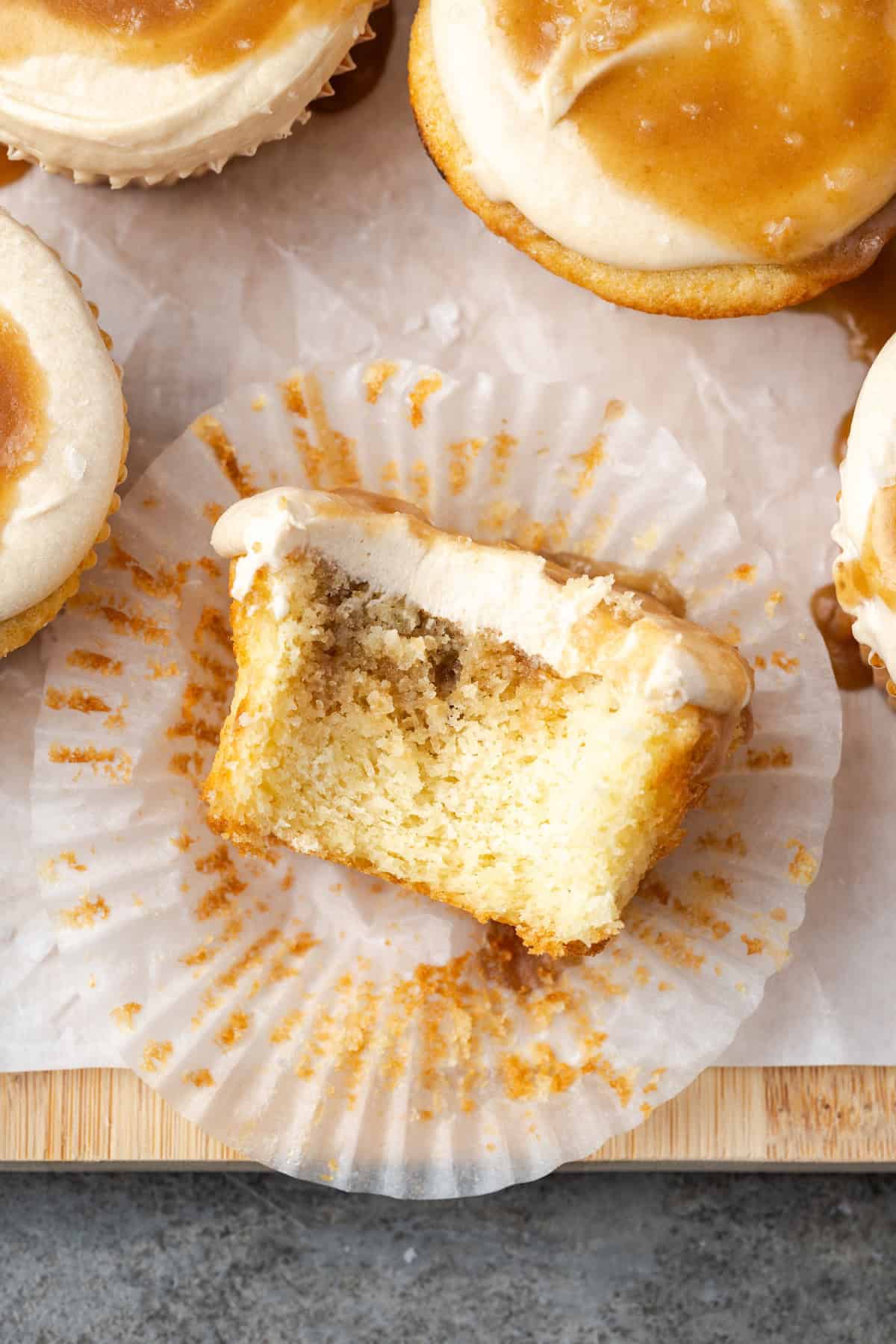 Overhead view of a salted caramel cupcake with a bite missing, resting in a cupcake wrapper next to more cupcakes.