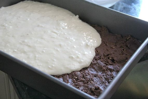 Coconut cream cheese batter being spread over chocolate cake batter in a 9x13 pan