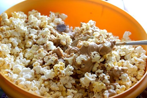 Melted peanut butter chips being mixed into popcorn and mini peanut butter cups in a bowl