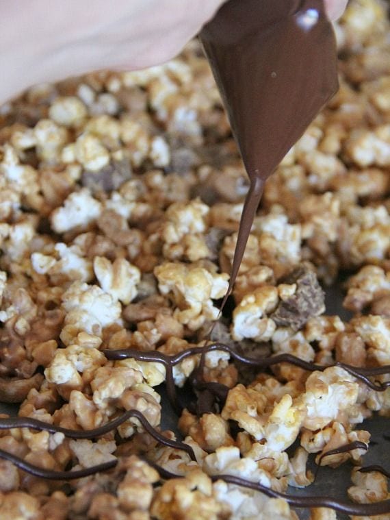 Melted chocolate being drizzled over peanut butter popcorn
