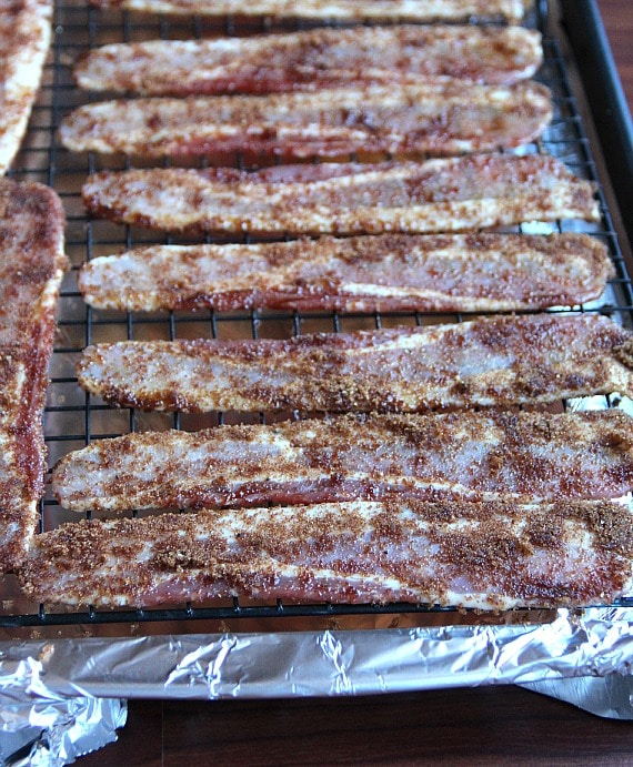 Raw bacon coated with brown sugar on a cooling rack inside a foil-lined baking sheet