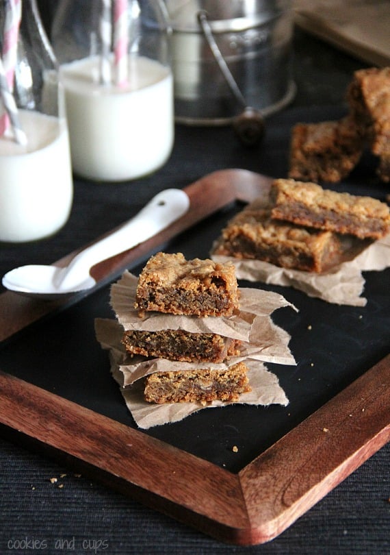 Several squares of brown sugar toffee bars on parchment paper with two glasses of milk