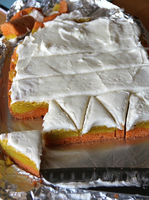 Orange, yellow and white layered frosted cookie bars being cut into triangles