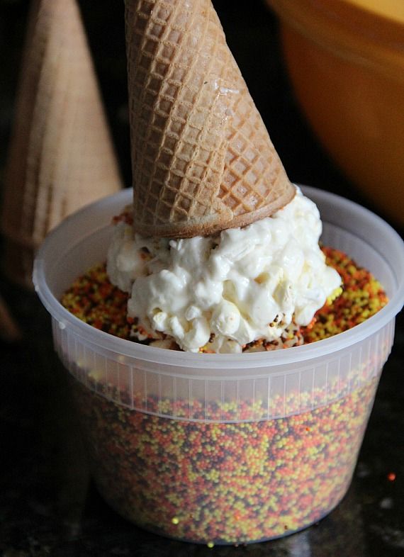 A popcorn ball ice cream cone being dipped in sprinkles
