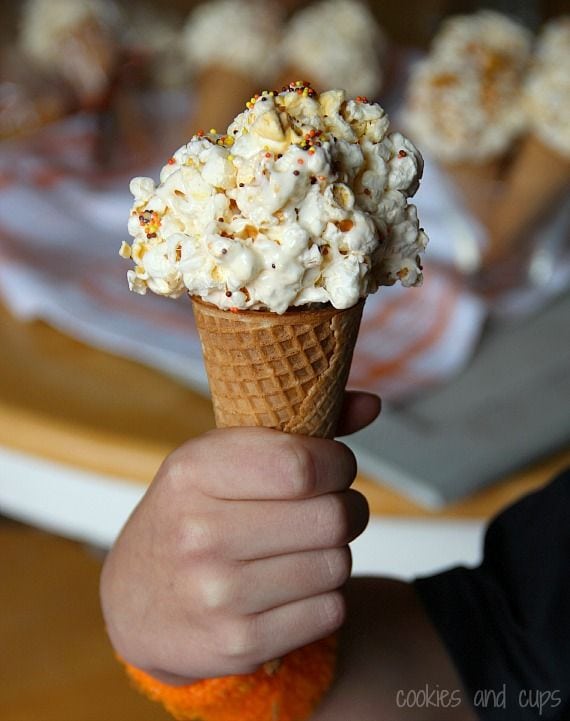 A hand holding a popcorn ball ice cream cone