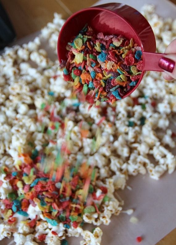 Fruity Pebbles being added to kettle corn with melted white chocolate