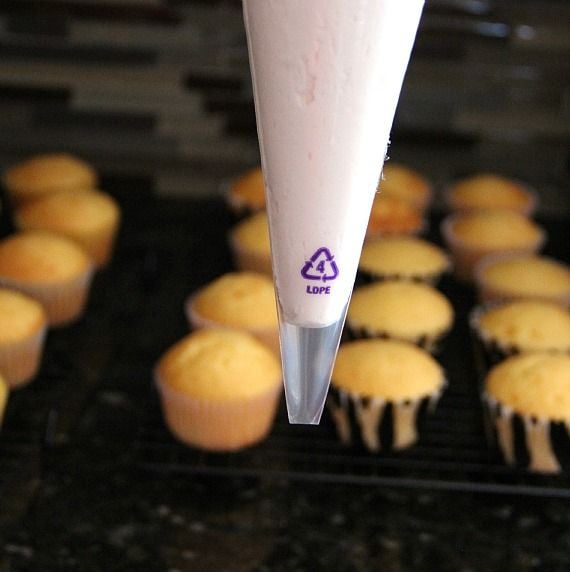 Marshmallow creme in a piping bag in front of vanilla cupcakes