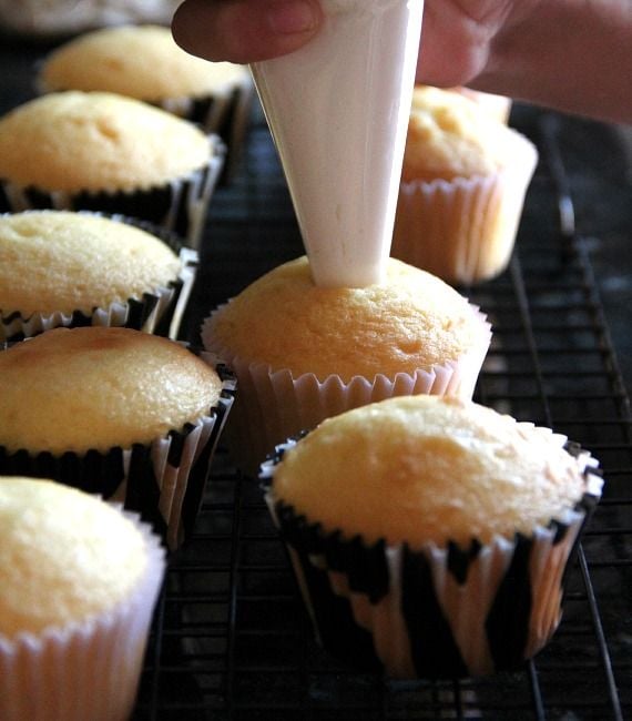 Vanilla cupcakes being filled with marshmallow creme from a piping bag