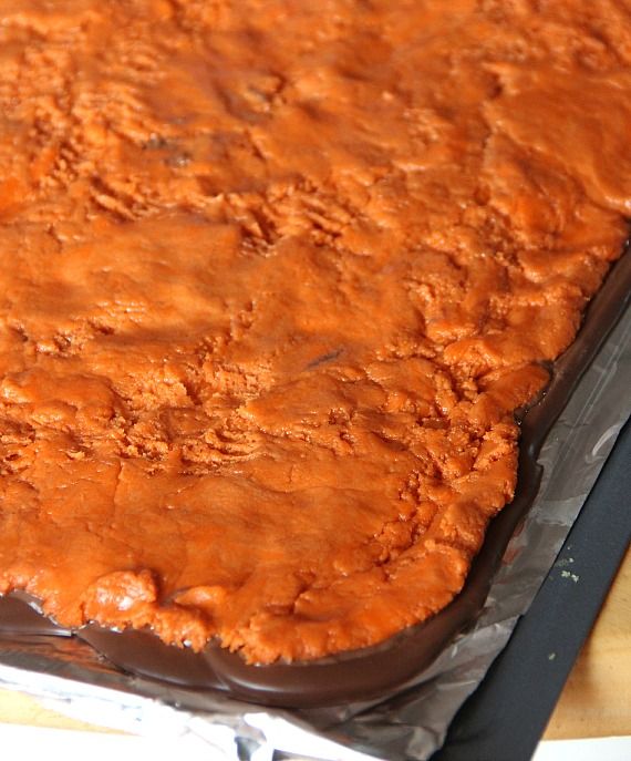 Homemade butterfinger filling spread over chocolate on a sheet pan