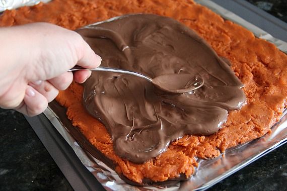 Chocolate being spread over homemade butterfinger filling in a sheet pan