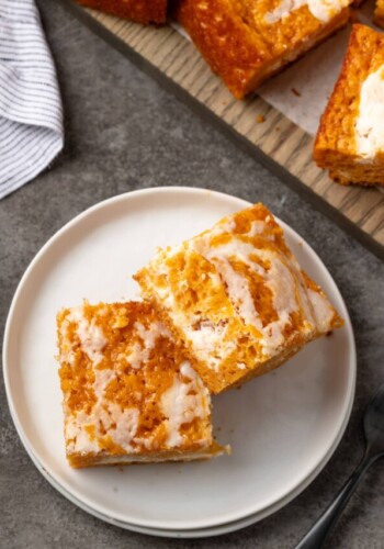 Overhead view of two pumpkin cream cheese bars on a white plate next to more bars on a wooden board.