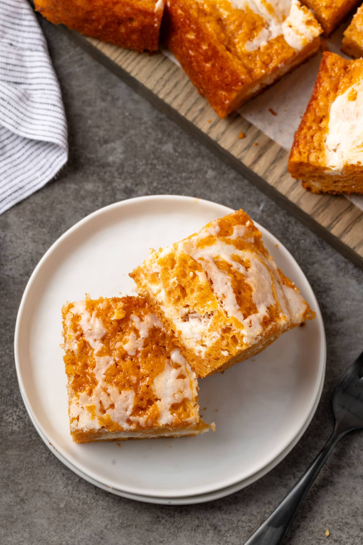 Overhead view of two pumpkin cream cheese bars on a white plate next to more bars on a wooden board.