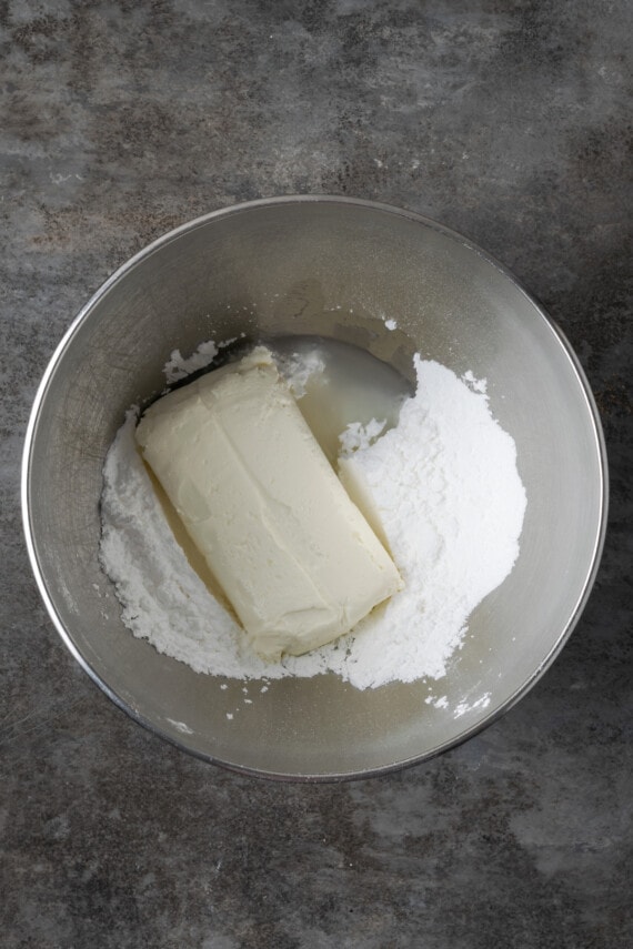 Cream cheese and powdered sugar combined in a metal mixing bowl.