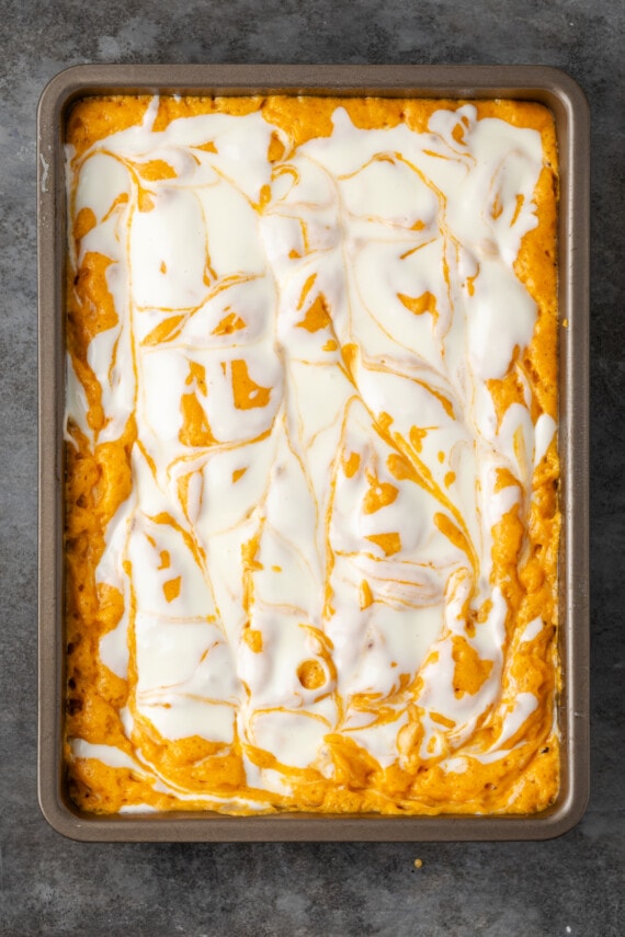 Unbaked pumpkin bar batter swirled with cream cheese in a baking pan.