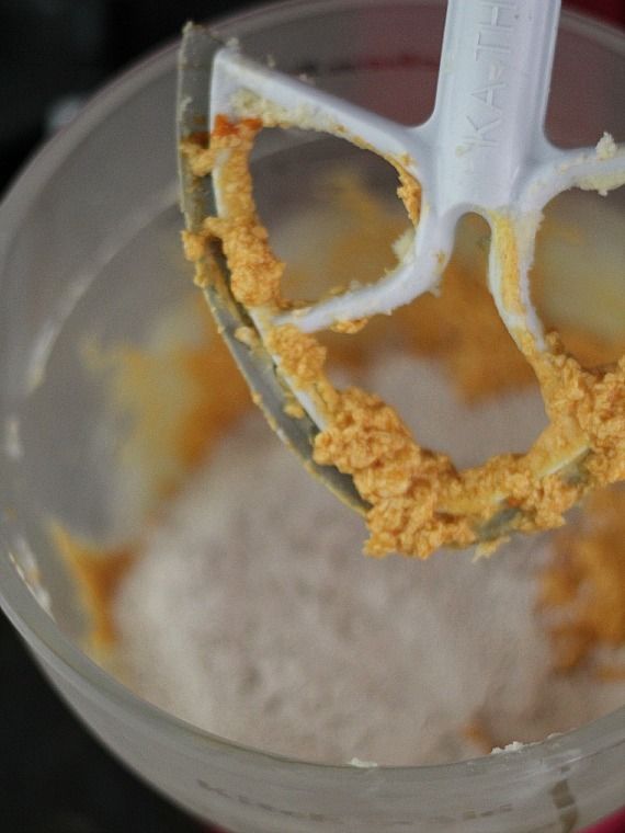 A stand mixer paddle attachment covered in cupcake dough, above a stand mixer bowl