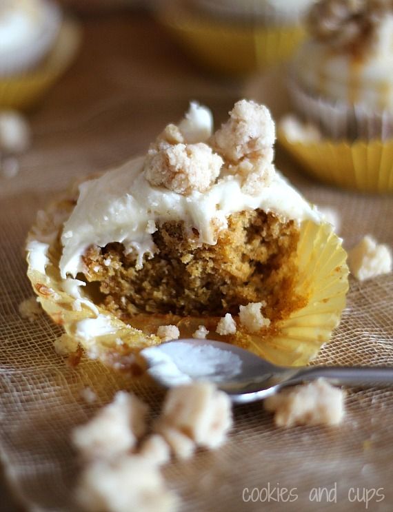 A half-eaten pumpkin cupcake topped with cream cheese frosting and streusel, with a spoon in front of it