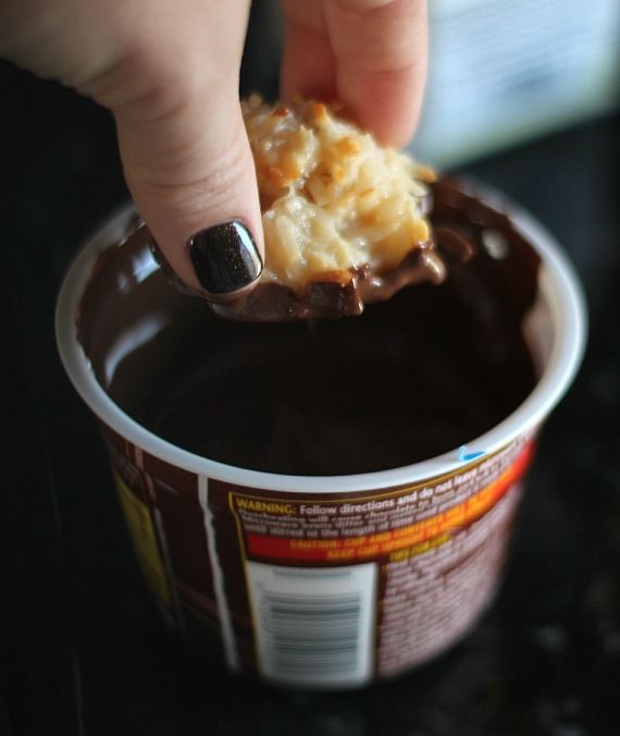 A coconut macaroon being dipped in melted chocolate