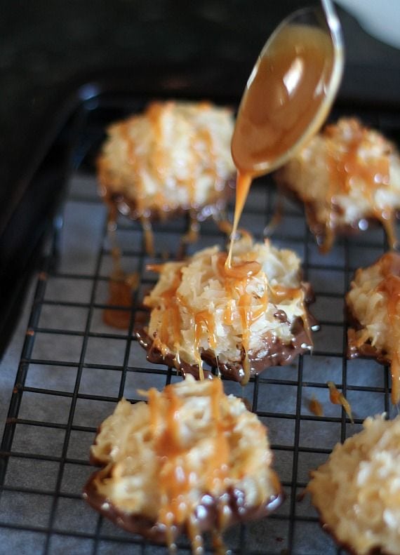 Caramel being drizzled over chocolate dipped coconut macaroons on a cooling rack