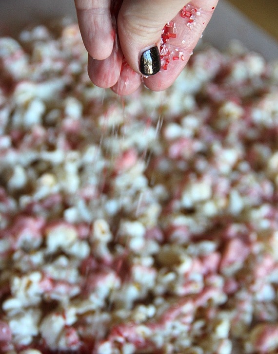 Red and white coarse sugar being sprinkled over popcorn