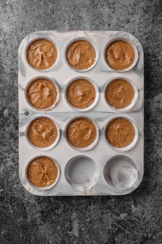 A lined cupcake pan filled with gingerbread cupcake batter.