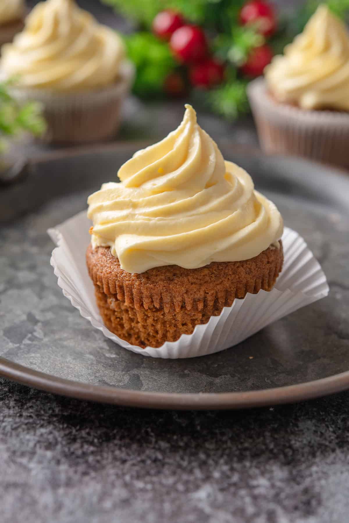 Close up of a partially unwrapped frosted gingerbread cupcake on a platter.