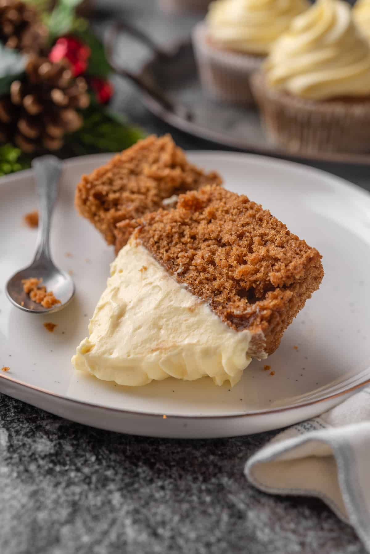 A frosted gingerbread cupcake cut in half on a white plate.