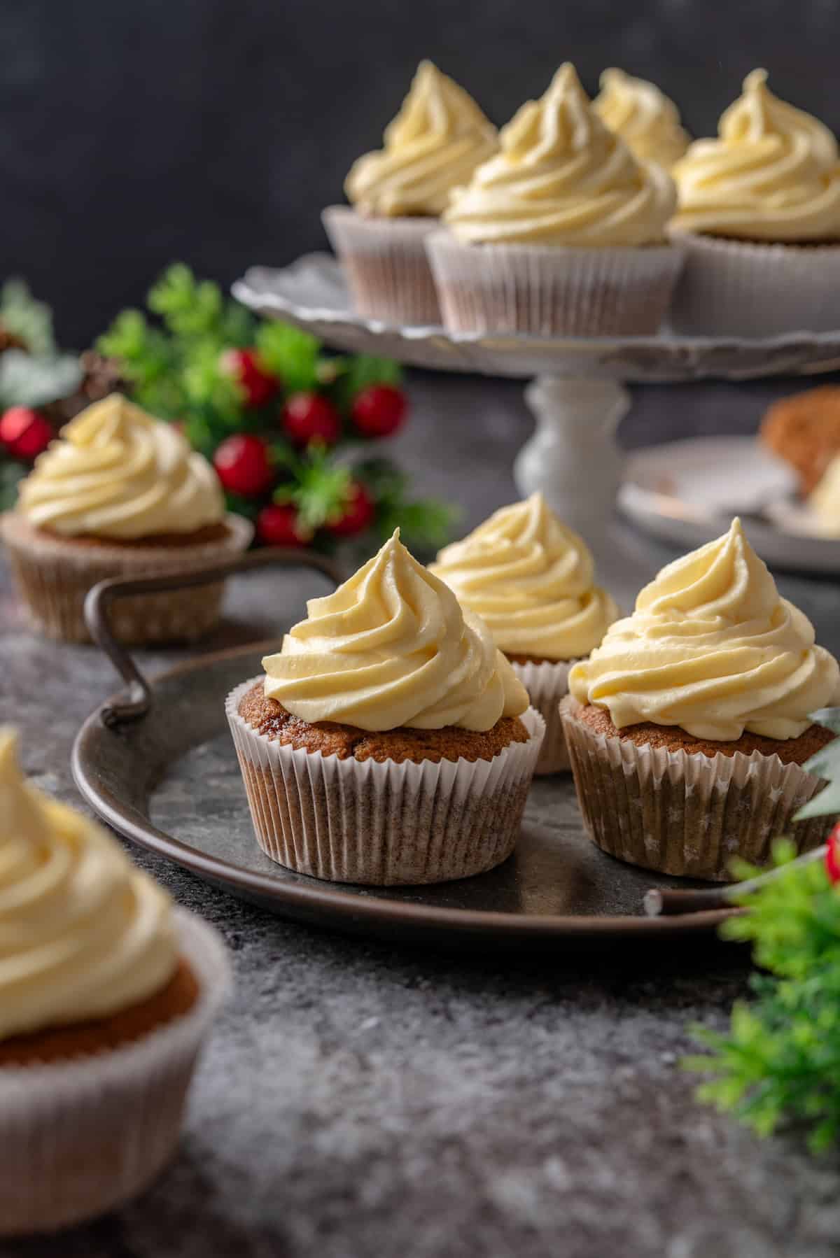 Frosted gingerbread cupcakes on a platter with more cupcakes on a cake stand in the background.