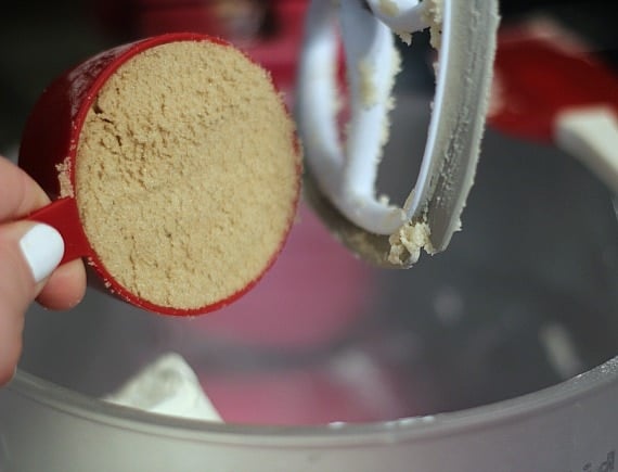 A measuring cup of brown sugar being added to a stand mixer bowl